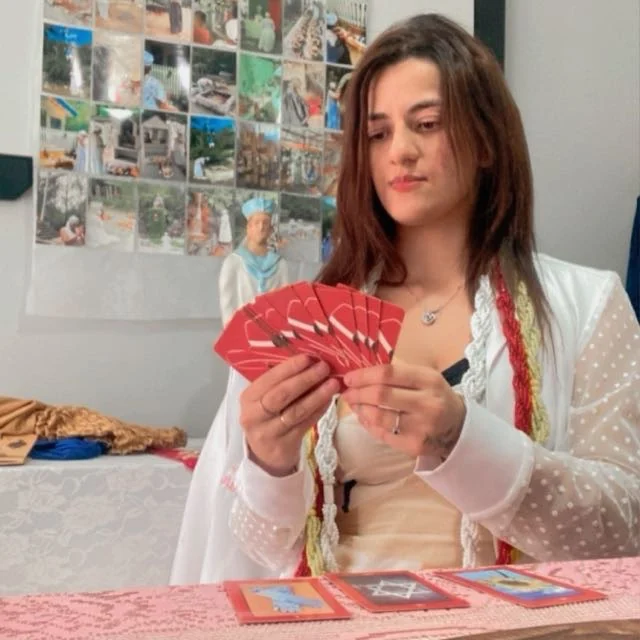 Mentora Kamily lendo tarô, com cartas vermelhas na mão e três cartas abertas sobre a mesa